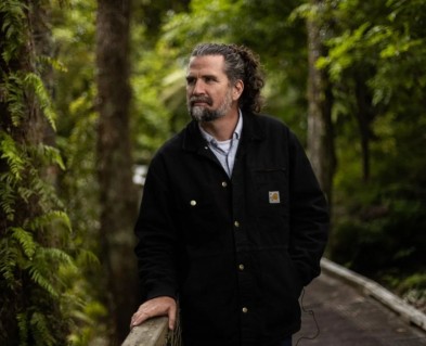 Tim Park, Ōtari Manager, standing on a wooden walkway in the forest. 